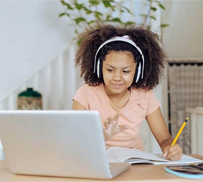 Elementary-aged female working on a laptop with headphones on