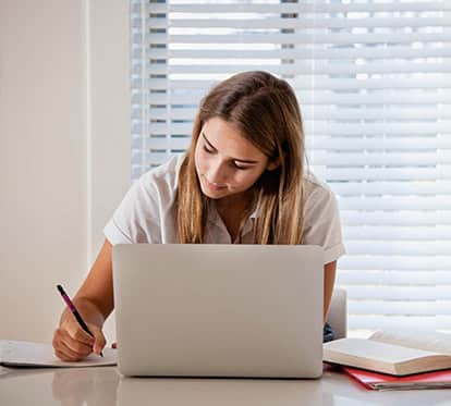 Female teenager in a white shirt doing schoolwork on a laptop