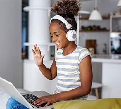 Middle school aged student with headphones on waving to someone on a video call