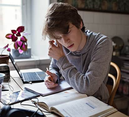 male teenager taking notes while taking online class